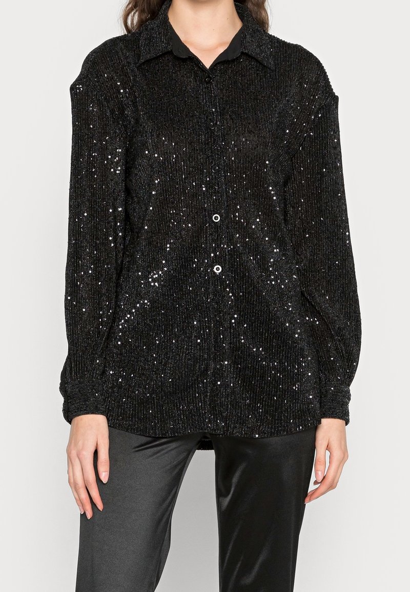 Black sequined button-up shirt with a collared neckline, ribbed texture, long sleeves, and a loose fit, paired with black pants.