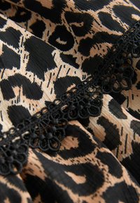 Tissu imprimé léopard beige et noir avec une bordure en dentelle noire ornée de motifs floraux et en boucles.