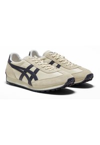 Sneaker in suede beige con dettagli e lacci in pelle blu scuro, dotate di una suola in gomma testurizzata con modelli di trazione visibili.