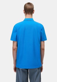 Blå pikétröja med texturerad tyg, korta ärmar och krage. Har en liten logotyp nära halsen och en rak fåll.