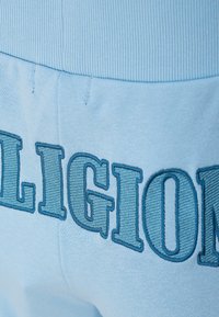 Joggers en coton bleu clair avec taille côtelée, ornés d'un grand texte en broderie "RELIGION" en bleu foncé au dos.