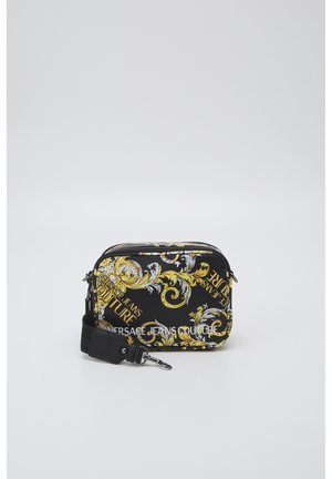 Mała czarna torebka na ramię z złotymi i białymi wzorami w stylu barokowym oraz napisem "Versace Jeans Couture", wyposażona w odpinany czarny pasek.