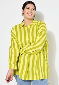 Camicia a maniche lunghe a righe verdi e gialle con una vestibilità rilassata. Tessuto texturizzato con colletto e spacchi laterali.