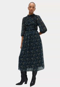 Sukienka o średniej długości w ciemnoniebieski wzór kwiatowy, z marszczonym dekoltem, bufiastymi rękawami, zestawiona z czarnymi botkami do kolan.