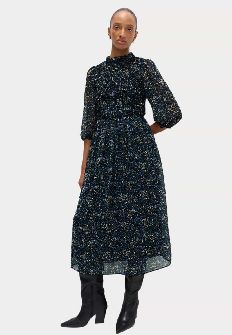 Sukienka o średniej długości w ciemnoniebieski wzór kwiatowy, z marszczonym dekoltem, bufiastymi rękawami, zestawiona z czarnymi botkami do kolan.