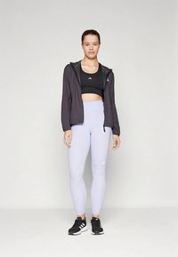 Svart atletisk crop-top, fiolette høytlivsleggings og en svart lett jakke med hette, kombinert med svarte joggesko.