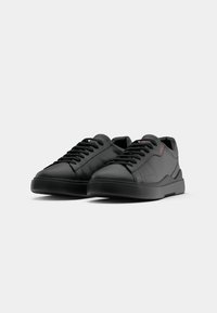 Baskets en cuir noir avec une finition lisse, bout rond, lacets plats et design minimaliste. Présentent un logo discret sur le côté.