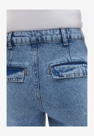 Světle modré džíny s vysokým pasem, které mají dvě zadní kapsy, jemné vyblednutí a kontrastní prošívání podél pásku a kapes.