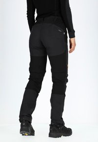 Zwarte outdoorbroeken met een slimfit ontwerp, voorzien van versterkte knieën en manchetten, en een combinatie van matte en lichtglanzende texturen.