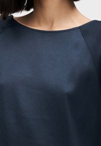 Haut bleu marine en tissu doux avec une texture lisse, doté d'un large col rond et de manches raglan courtes.