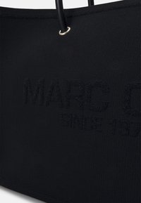 Sac fourre-tout noir texturé avec poignées rondes noires et texte embossé subtil indiquant "MARC O" et "SINCE 19".