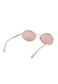 Lunettes de soleil rondes teintées de rose avec des montures fines en or et des branches roses, présentées en angle sur un fond blanc.