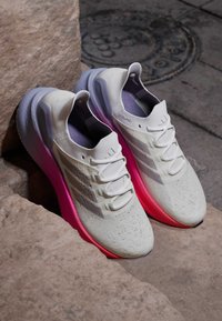 Scarpe da ginnastica bianche con suola a gradiente rosa, tomaia in rete, dettagli testurizzati e design a tre strisce ai lati. Forma della punta arrotondata.