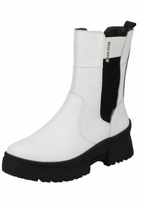White ankle boots made of smooth material, featuring black elastic side panels and a chunky black sole with textured tread for grip.
