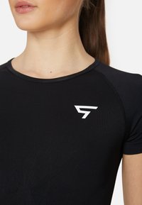 Maglietta sportiva nera a maniche corte con scollo rotondo e un logo bianco sul petto. Il tessuto ha una texture liscia e aderente.