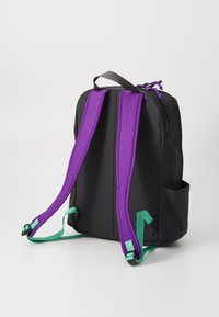 Svart ryggsekk med lilla polstrede stropper og grønne detaljer. Har robust materiale, et enkelt design og side lommer for oppbevaring.