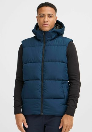 Navy blue padded vest with a high collar and hood, featuring a front zipper and side pockets. Textured fabric with quilted sections.