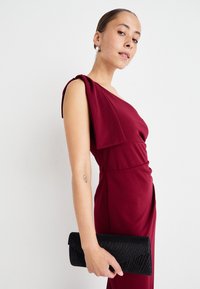 Burgunderfarget kjole med asymmetrisk design med én skulder, drapert stoff, tettsittende midje, og en svart clutch med teksturert mønster og slank silhuett.