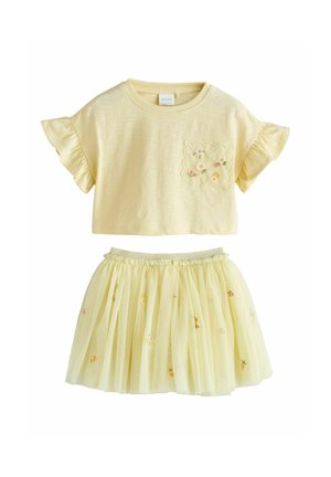Żółty dwuczęściowy strój składający się z topu z krótkim rękawem i falbanami oraz haftem kwiatowym, połączony z piętrową, haftowaną spódnicą z tiulu.