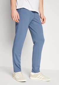 Světle modré tepláky vyrobené z měkkého materiálu se slim fit střihem. Design obsahuje boční kapsy a žebrované manžety; nošeny s krémovými teniskami.