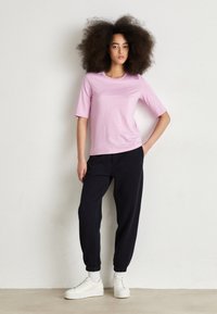 Ljusrosa t-shirt med kort ärm, kombinerad med marinblå joggarbyxor och vita sneakers. Enkel design, gjort av bomull och med elastiska muddar.