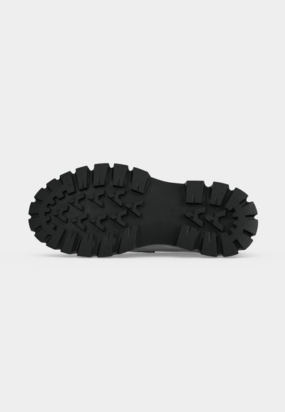 Semelle de botte noire robuste avec des crampons profonds et épais ainsi que des motifs anguleux conçue pour une forte adhérence et une utilisation en extérieur.