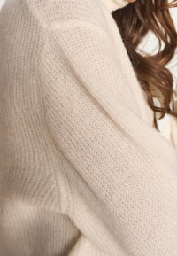 Vaaleanbeige neulepaita pehmeällä, teksturoidulla pinnalla. Siinä on resorireunukset ja rento istuvuus. Materiaali vaikuttaa mukavalta ja hengittävältä.