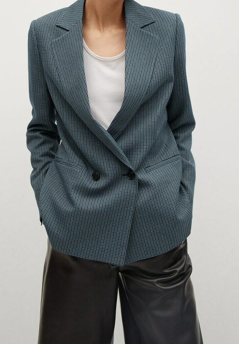 Blazer croisé en tissu tartan teal, avec un col à revers, des épaules structurées et de grandes poches latérales. Assorti à un top blanc.