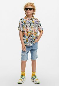 Camicia a maniche corte con un motivo cartoon colorato, abbinata a pantaloni corti in denim strappati, calze gialle e sneakers a fantasia.