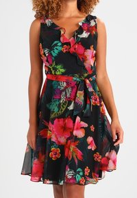 Kwiatowa sukienka na czarnym tle, z żywymi różowymi, czerwonymi i zielonymi wzorami; falbaniasty dekolt oraz wiązany w pasie. Sylwetka w kształcie litery A.
