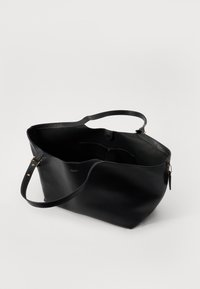 Sac fourre-tout en cuir noir avec une bandoulière, ouverture sur le dessus, poche intérieure et accents en métal doré. Texture lisse, design minimaliste.