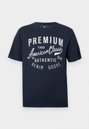 T-shirt en coton bleu marine avec texte blanc imprimé : « PREMIUM 1990 American Classic Authentic Denim Goods » en polices variées.