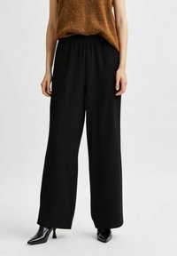 Pantalons larges noirs avec une taille élastique. Associés à un haut sans manches marron clair et des bottes à talons noires brillantes pour un contraste.