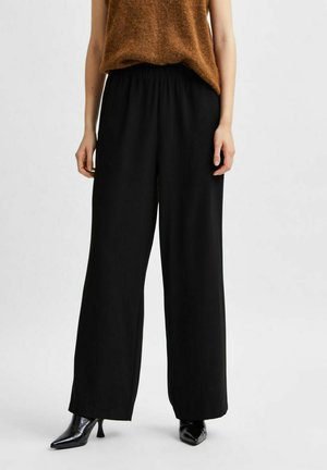 Zwarte broek met wijde pijpen en een flexibele tailleband. Gestyld met een lichtbruine mouwloze top en glanzende zwarte hakken voor contrast.
