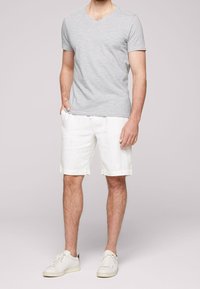T-shirt gris à manches courtes avec col en V, associé à un short en lin blanc, complété par des baskets blanches. Design simple et décontracté pour une tenue d'été.