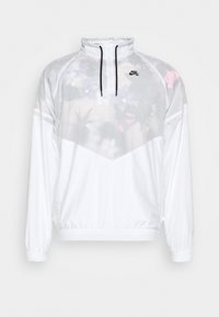 Giacca bianca Nike con stampa floreale, mezza zip, polsini elasticizzati e vestibilità rilassata. Realizzata in materiale leggero e traspirante.