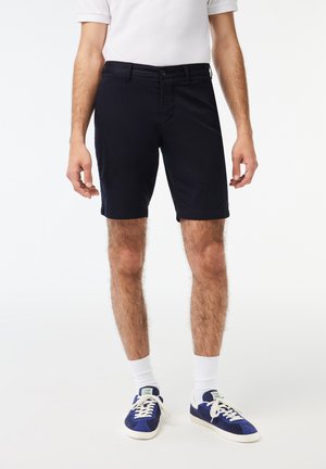 Pantaloni corti in cotone blu navy con una vestibilità dritta e orlo rigirato. Presenta una chiusura con bottone e zip davanti, con tasche laterali e posteriori.