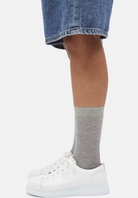 Zapatillas blancas de cuero con suela gruesa, combinadas con calcetines gris claro acanalados hasta la mitad de la pantorrilla, usadas con una falda de mezclilla. Vista en primer plano.