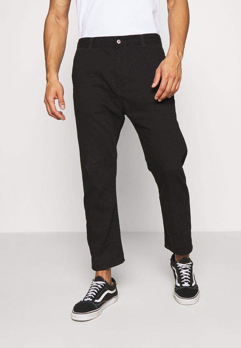 Černé bavlněné kalhoty s rovně střiženým střihem, s jemným leskem a předními kapsami. V kombinaci s černo-bílými teniskami.