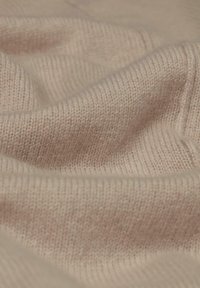 Helles beige gestricktes Gewebe mit weicher Textur, das über ein feines Rippmuster und sanfte Drapierungen verfügt und so ein gemütliches Erscheinungsbild schafft.