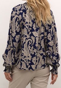 Blouse bleu marine avec un motif cachemire floral beige complexe. Dotée de manches longues et amples avec poignets smockés, fabriquée en tissu léger.