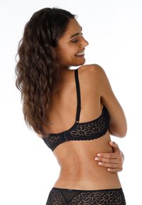 Brassiere in pizzo nero con motivo floreale, spalline regolabili e chiusura posteriore a gancio. Texture dettagliata con bordi a scalloped e morbida fodera.