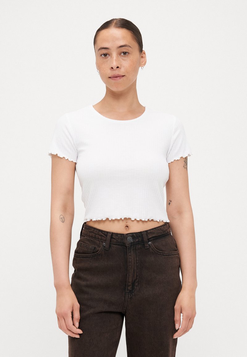 Biely rebrovaný crop top s krátkymi rukávmi a vlnkovými okrajmi, skombinovaný s tmavo hnedými kapsáčmi s vysokým pásom. Jednoduchý a priliehavý dizajn.