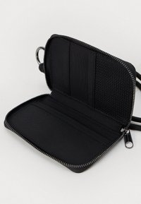 Juodas užtrauktuku užsegamas piniginė, išskleista plokščiai, su kortelių kišenėmis ir tinkleliu viduje, ant balto fono.