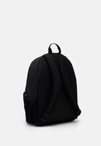 Black fabric backpack with padded straps, a top handle, and a side mesh pocket. Features a curved, structured shape.