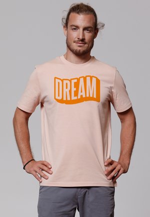 Korte mouwen perzikkleurig T-shirt met een vet, gebogen "DREAM" graphic in oranje. Zacht materiaal met een ronde hals en een relaxte pasvorm.