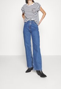 Camiseta de rayas de manga corta con un bolsillo en el pecho, combinada con jeans de pierna ancha azul y botas de tacón negro hasta el tobillo.