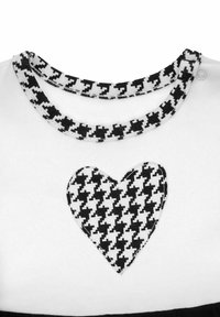 Biała koszula z kołnierzem w czarno-biały wzór pepitki oraz naszywką w kształcie serca z tego samego wzoru na przodzie. Gładka tekstura, casualowy design.