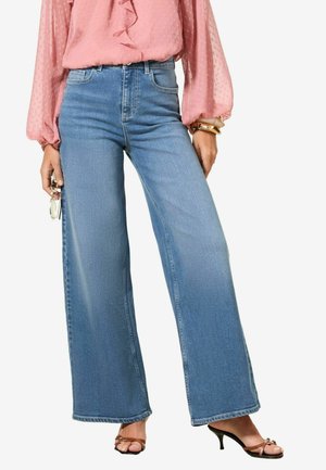 Light blue high-waisted wide-leg jeans with a classic denim finish. Paired with a pink ruffled blouse and strappy black heeled sandals.