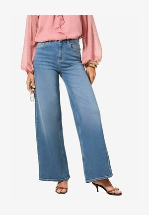Lichtblauwe high-waisted wide-leg jeans met een klassieke denimafwerking. Gepaard met een roze blouse met ruffles en zwarte sandalen met hakken en bandjes.